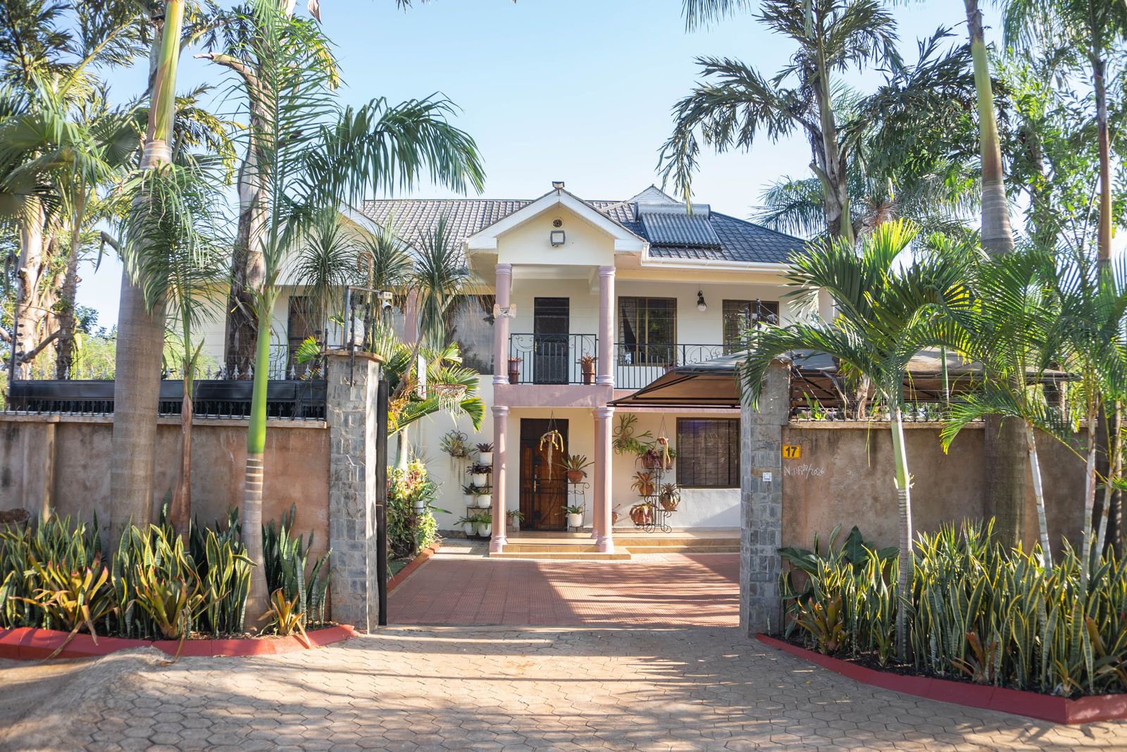 Two-storey cream house with palms behind a gated paved drive, the JJ Tanzania Homes Cultural Home